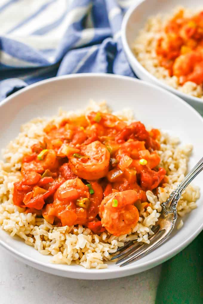 A fork resting in a low white bowl with brown rice topped with shrimp creole.