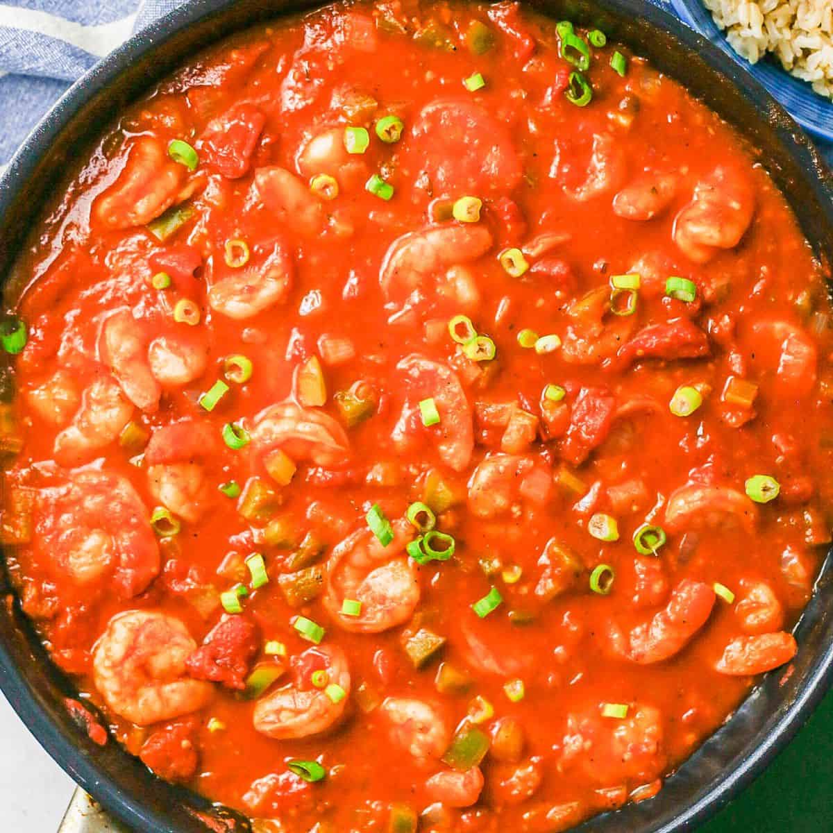 Saucy shrimp creole in a dark skillet topped with green onions.