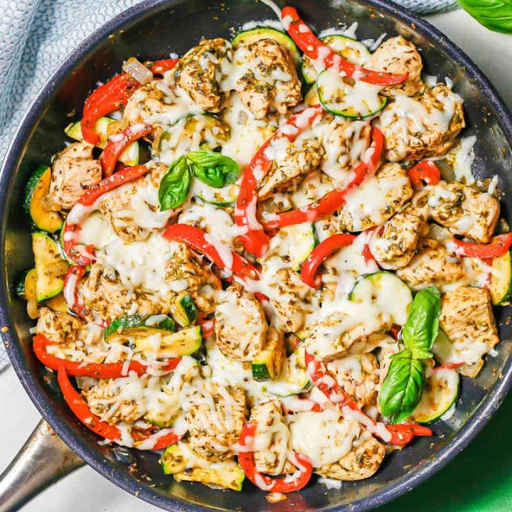 A mix of chicken and veggies in a large dark skillet topped with melted mozzarella cheese.