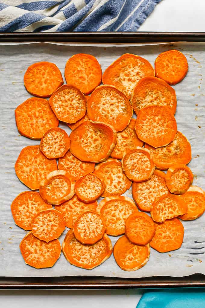 Round sweet potato slices on a parchment paper lined baking sheet after being baked.
