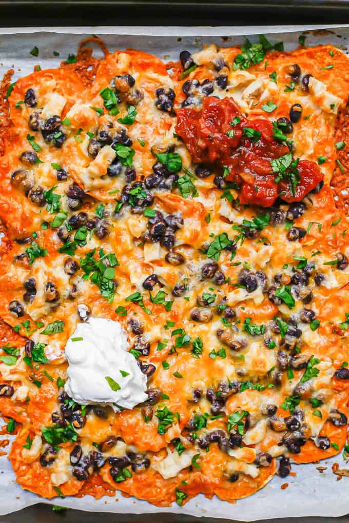 A baking sheet of cheesy nachos with sweet potatoes, black beans and chicken.
