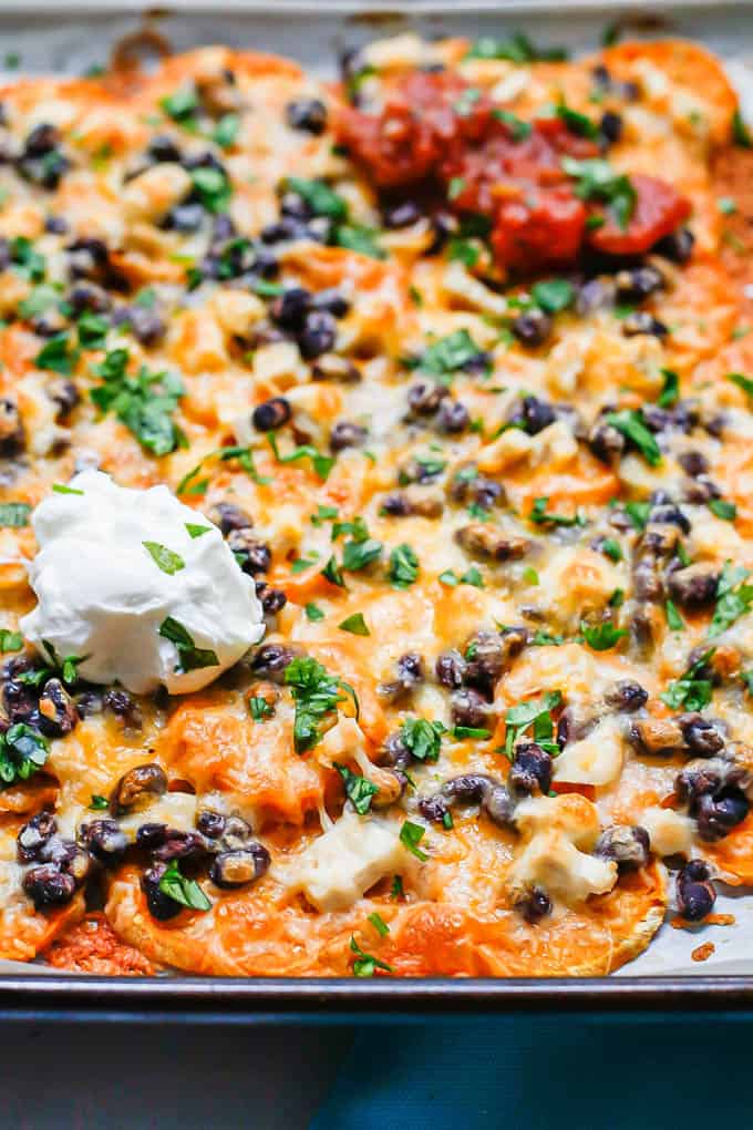 Sweet potato nachos on a baking sheet with chicken, beans, cheese and toppings.