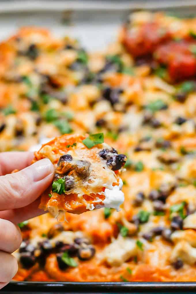 A hand holding up a loaded sweet potato nacho from a baking sheet.