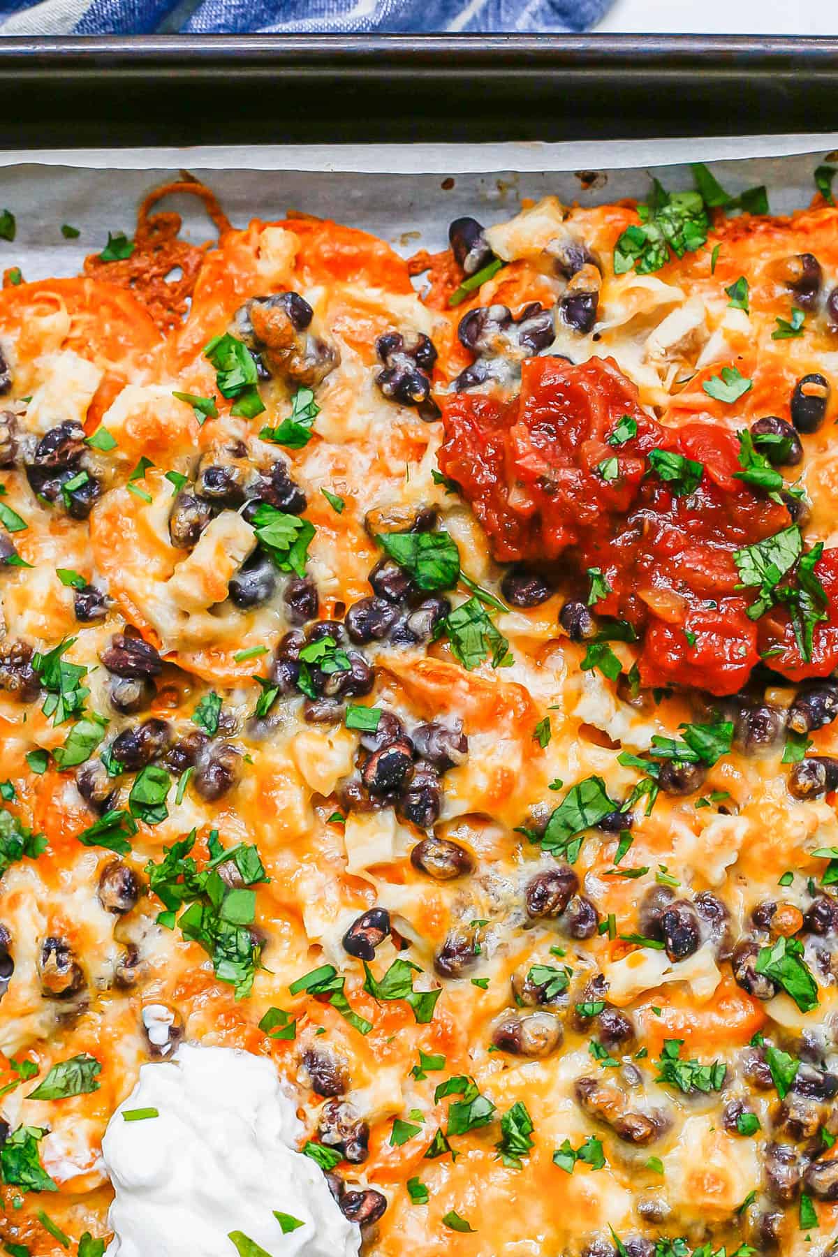 A sheet pan filled with sweet potato nachos topped with black beans, cheese, cilantro, salsa and sour cream.