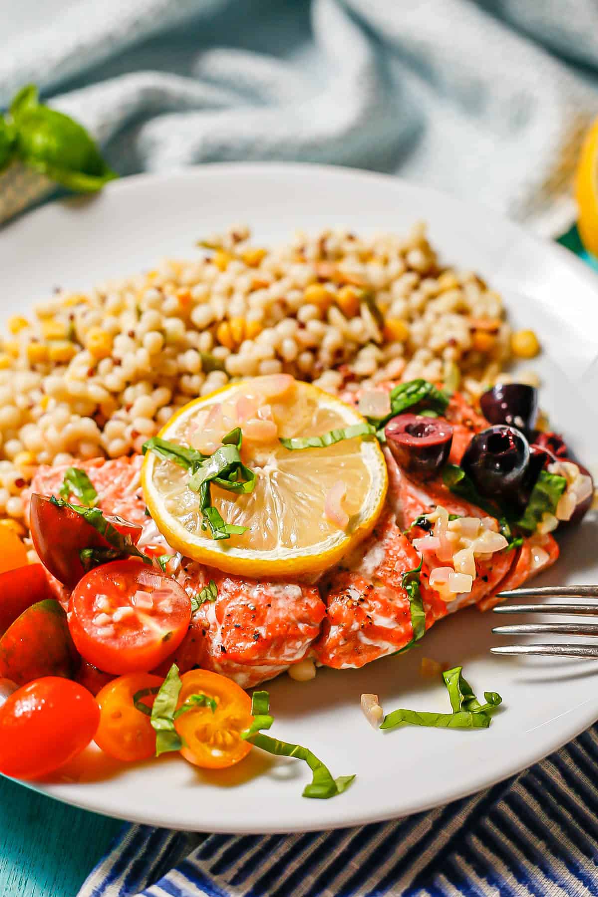 Baked Mediterranean salmon with lemon, basil, tomatoes and olives on a round white plate with a grain mix.