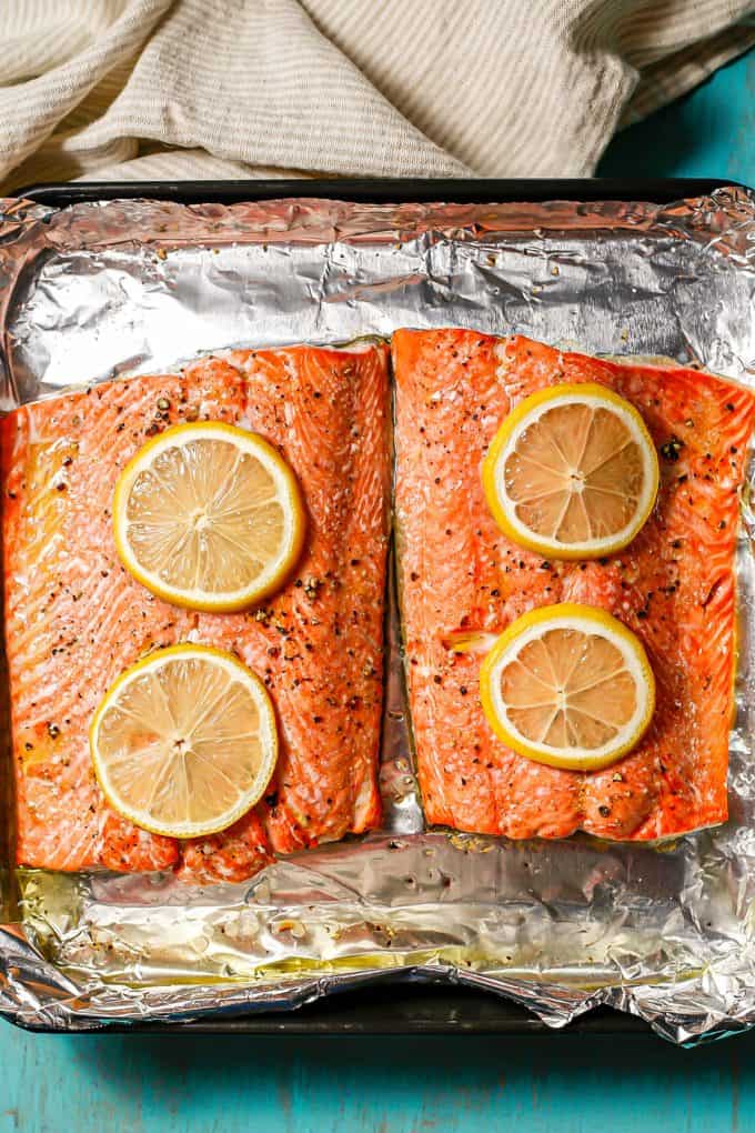 Two large salmon filets on a foil lined baking sheet topped with lemon slices after being roasted.