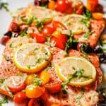 Large salmon filets topped with lemon slices, assorted colored tomatoes, olives, basil and a shallot dressing with a text overlay on the photo.