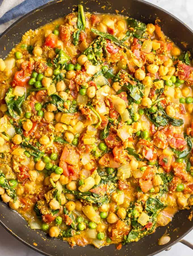 Square photo of a chickpea and veggie curry in a large dark skillet.