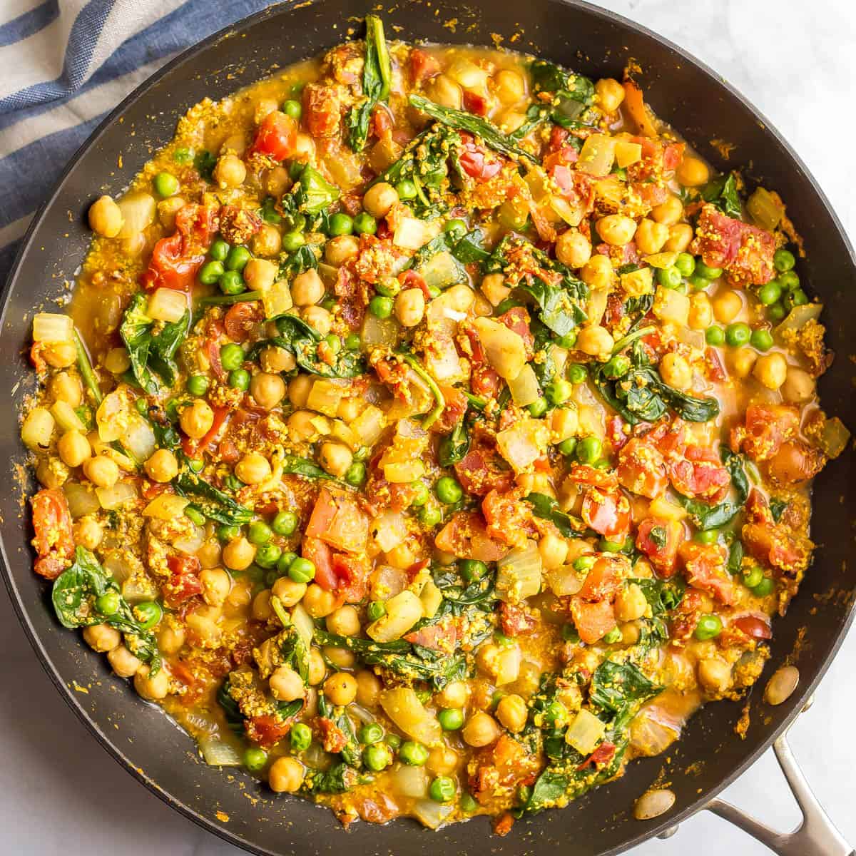 Square photo of a chickpea and veggie curry in a large dark skillet.