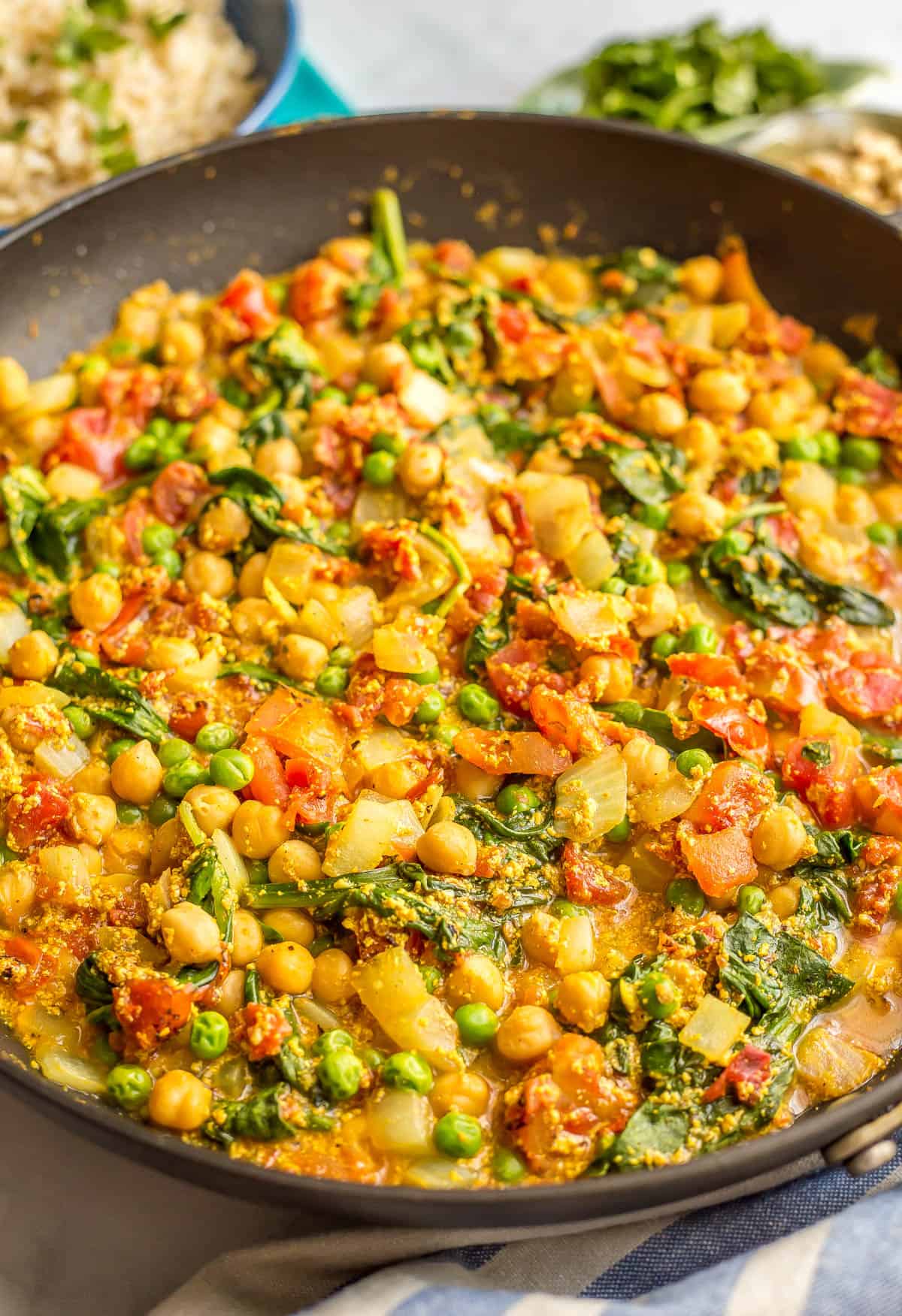 A vegetarian curry with chickpeas, peas, tomatoes and spinach in a large dark skillet.