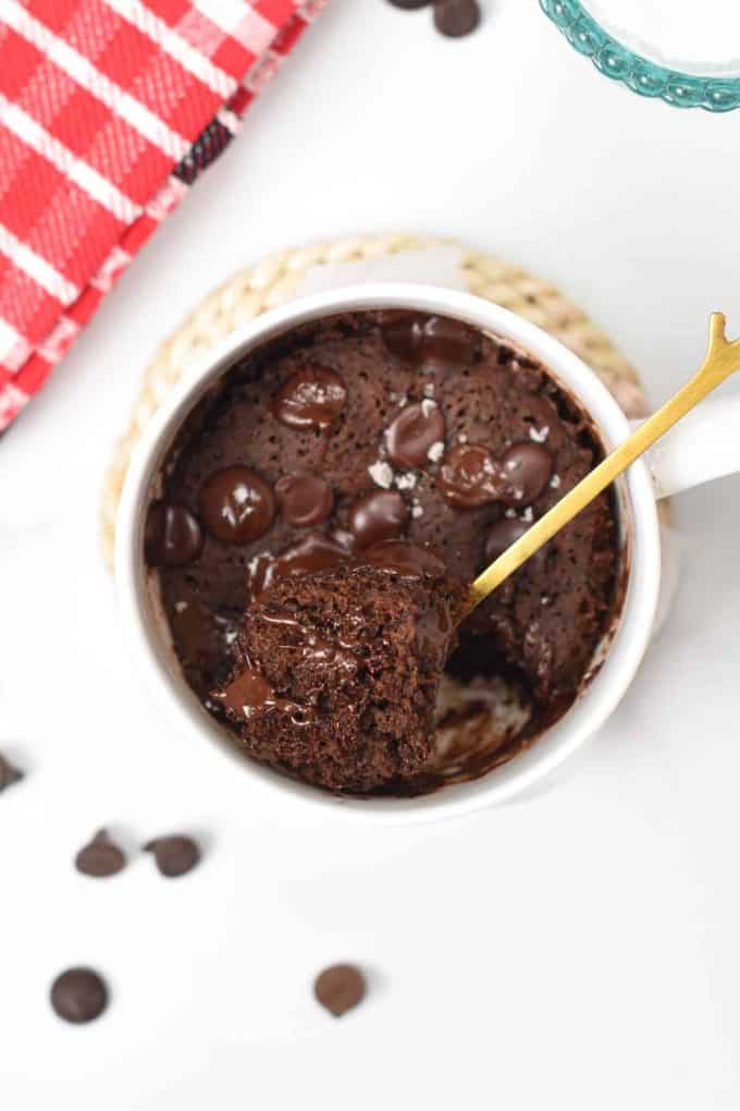 A spoon scooping up part of a healthy chocolate mug cake from a white mug.