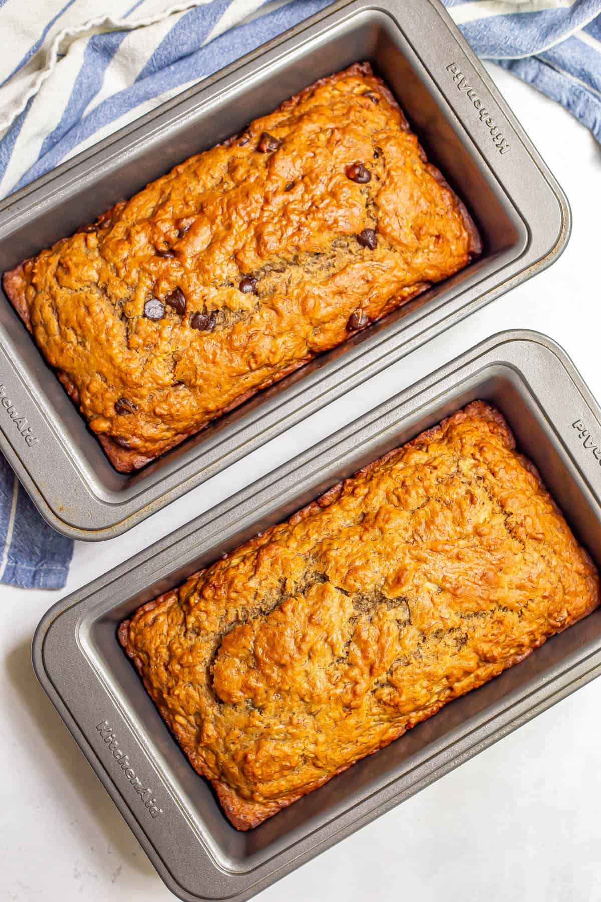Two baked loaves of healthy banana bread, one with chocolate chips, in pans.
