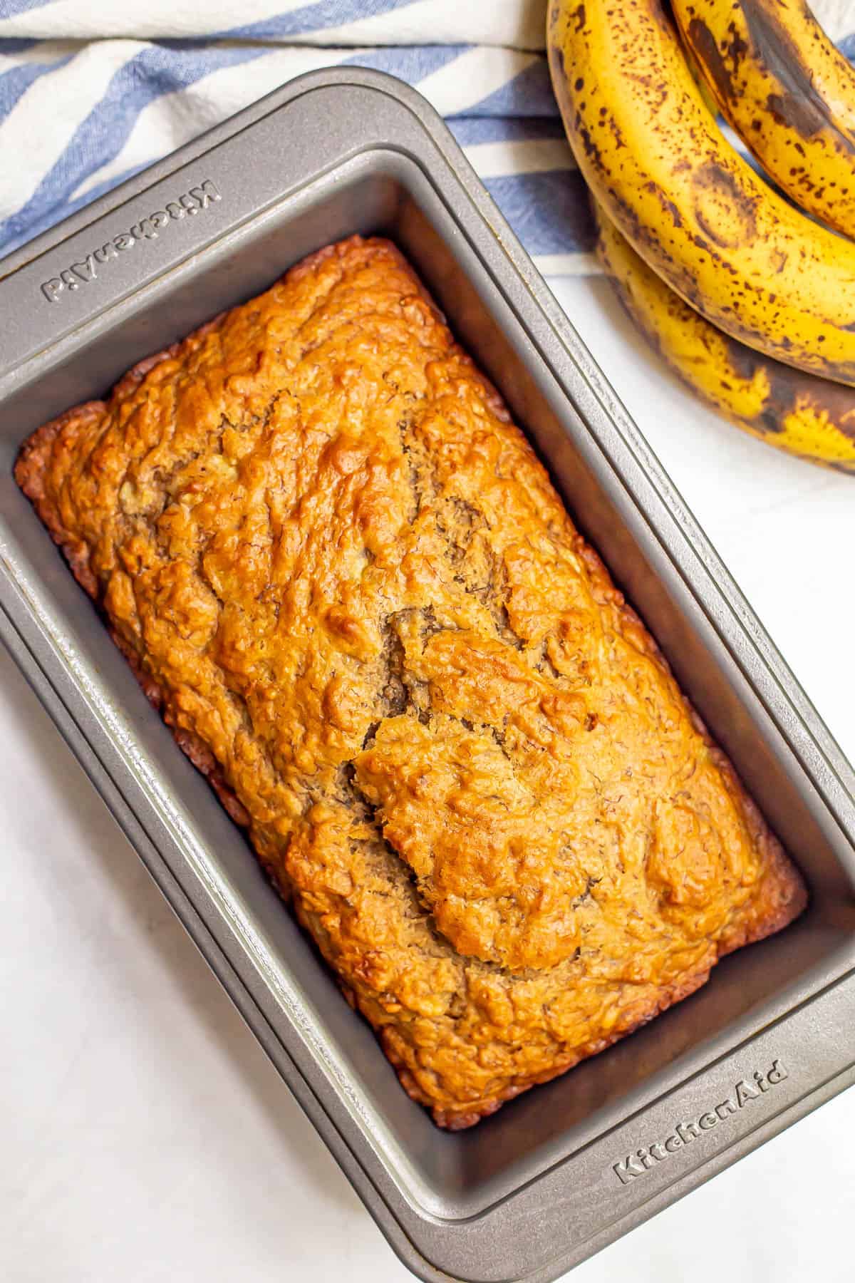 A pan with baked healthy banana bread with ripe bananas nearby.