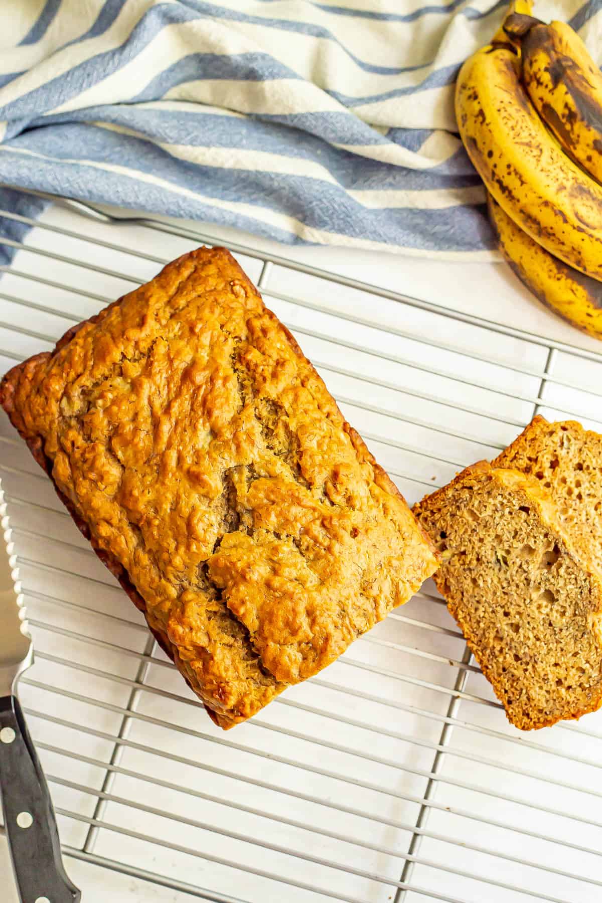 Whole grain banana bread on a cooling rack with a couple of slices cut.