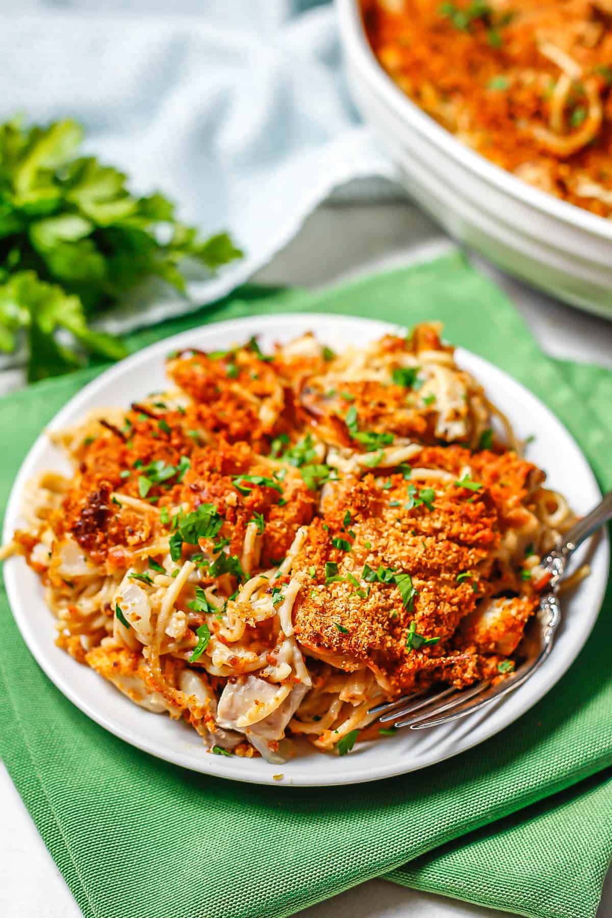 Healthy chicken tetrazzini served on a small round white plate with parsley sprinkled on top and a fork to the side.