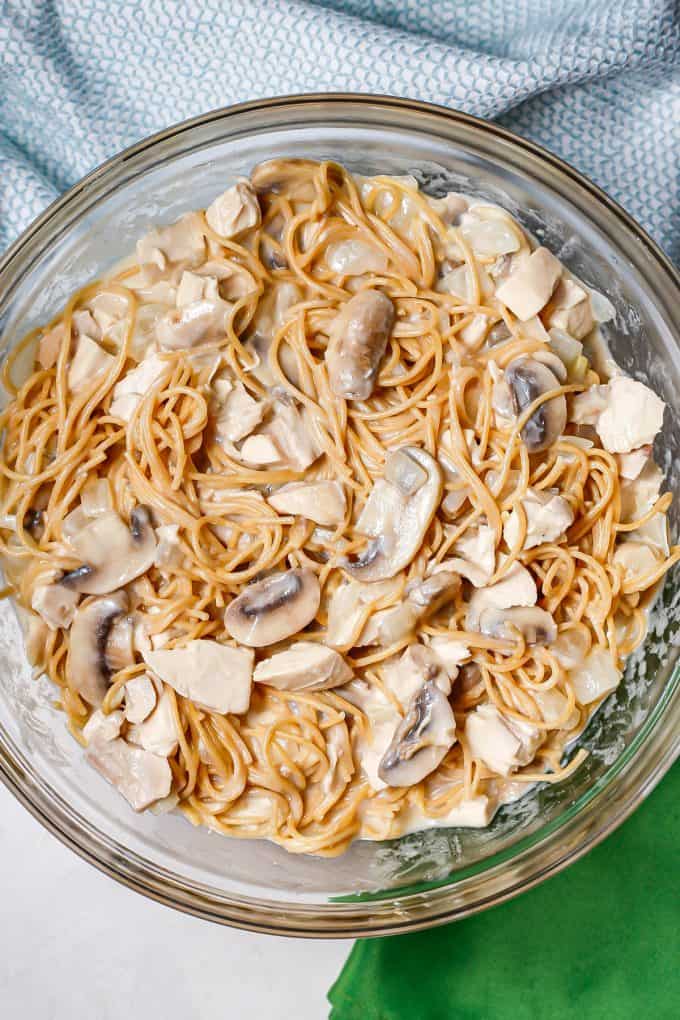 Spaghetti noodles mixed with chicken, mushrooms and a creamy sauce in a large glass bowl.