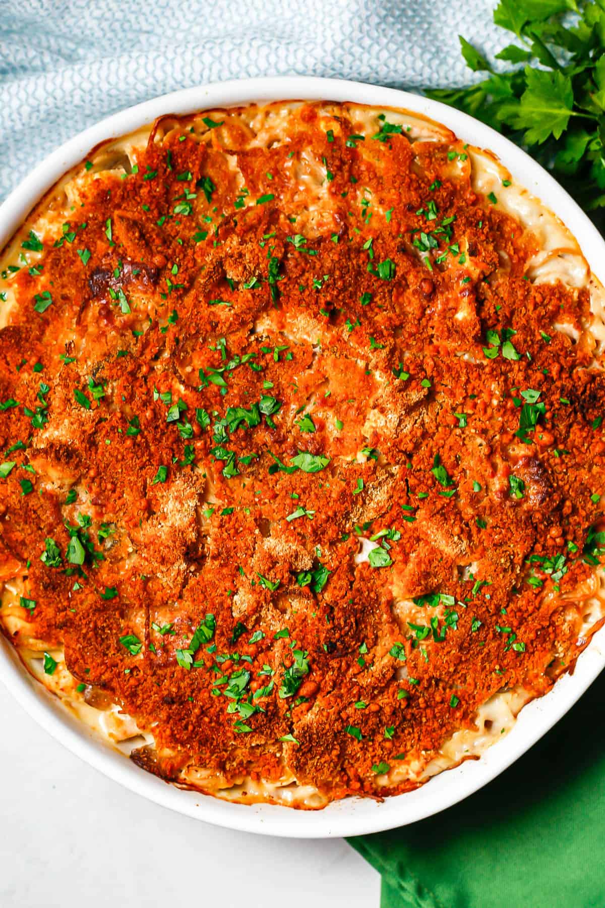 Creamy baked chicken tetrazzini in a round white casserole dish with a golden brown topping and parsley sprinkled on top.