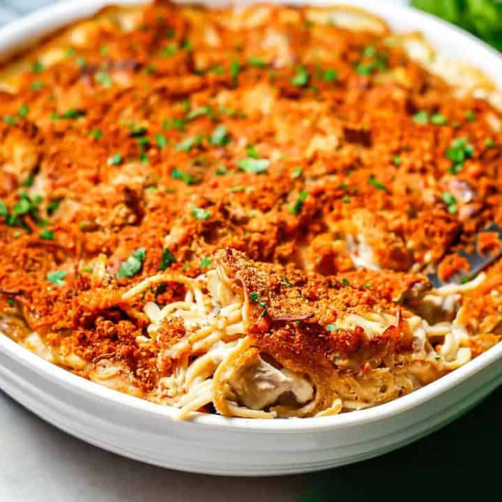 Close up of a scoop of chicken tetrazzini resting in a large round white casserole dish.