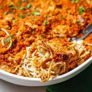 Close up of a scoop of healthy baked chicken tetrazzini in a large white casserole dish.