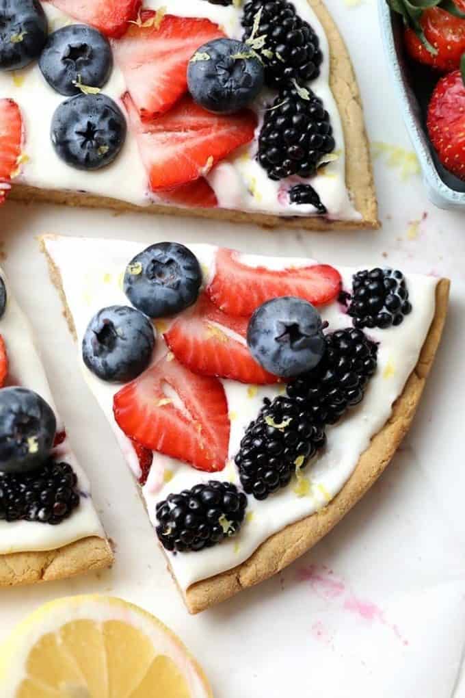 A slice of yogurt topped fruit pizza with berries pulled away from the pie.