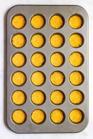 A mini muffin tin with all the cups with a graham cracker crust pressed in.