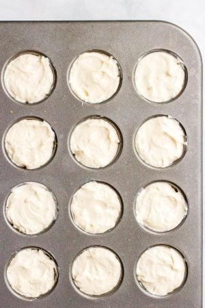 A mini muffin tin filled with a cheesecake mixture.