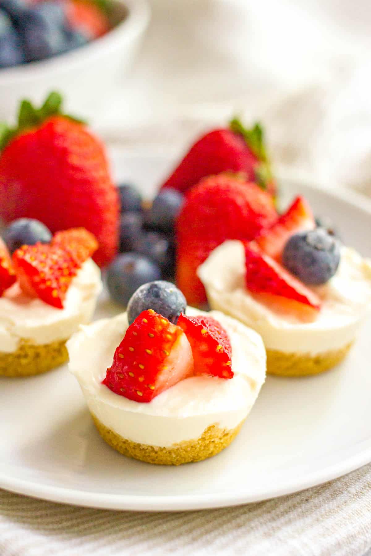 Mini cheesecake bites with a graham cracker crust and fresh fruit on top served on a small white plate.