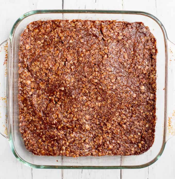 A chocolate oat cookie mixture pressed into an 8x8 glass pan.