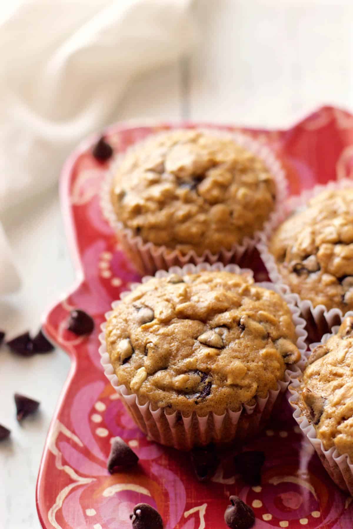 Healthy chocolate chip muffins on a red plate with chocolate chips scattered nearby.