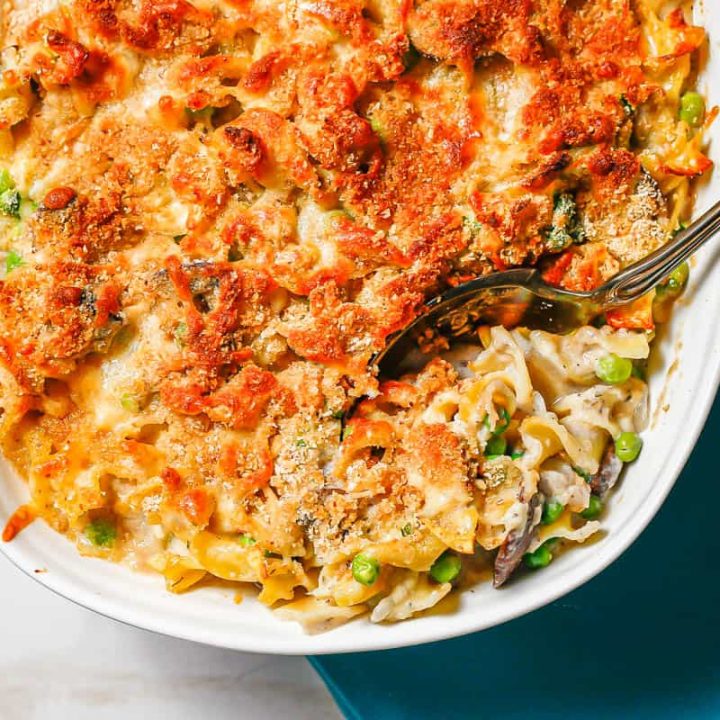 A scoop of a healthy tuna noodle casserole being taken from a white casserole dish.