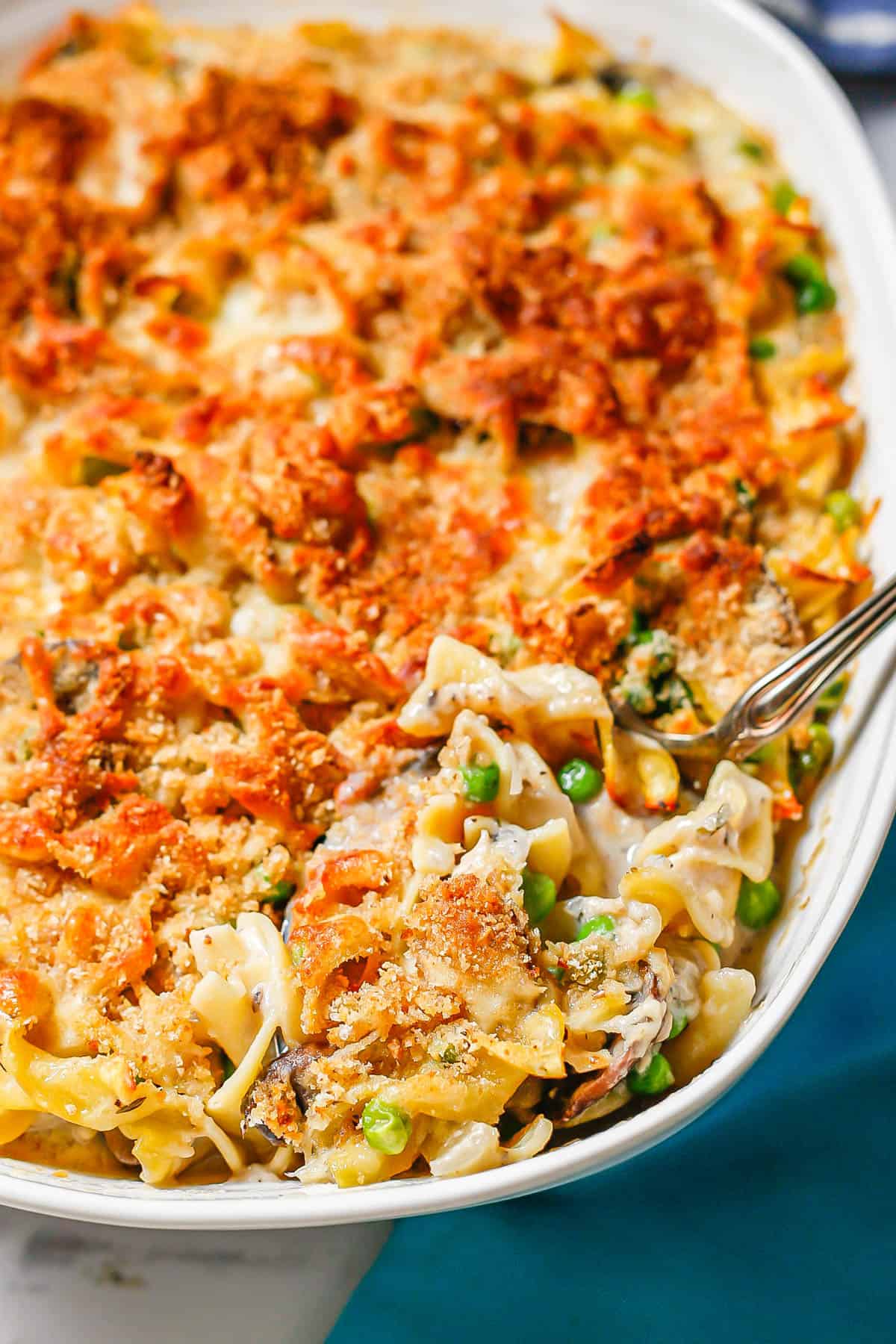 A scoop being taken out of a baked tuna noodle casserole with a crunchy browned breadcrumb topping.