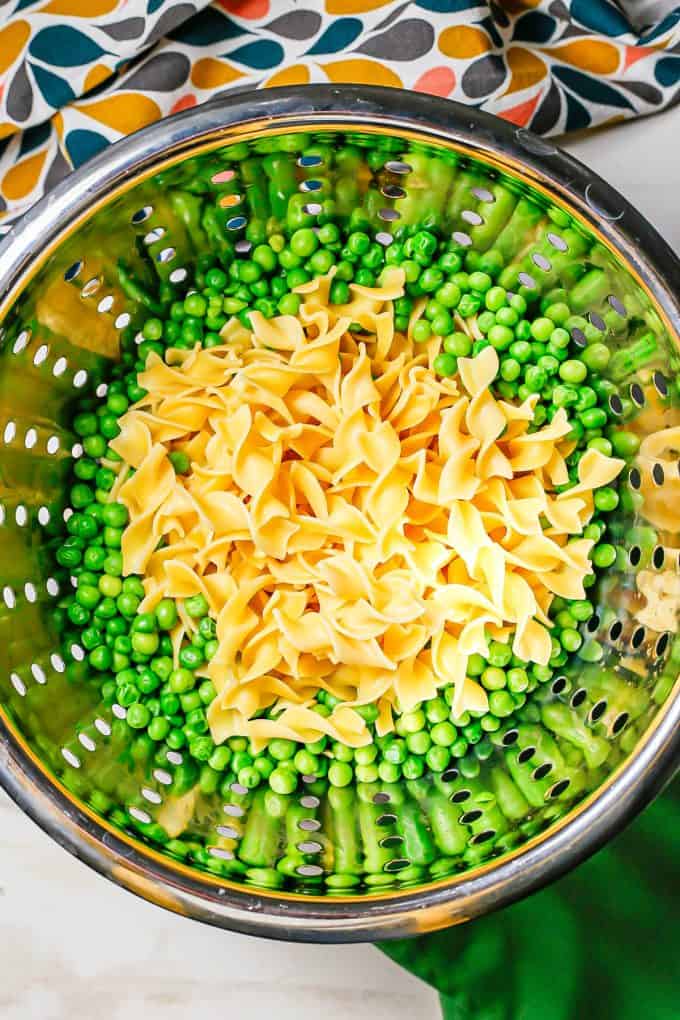 A silver colander with peas and egg noodles being drained.
