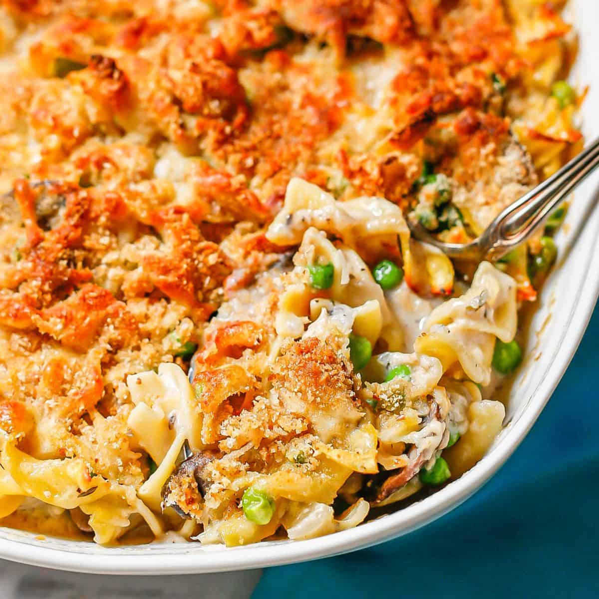 Close up of a scoop being taken out of a baked tuna noodle casserole with a crunchy browned breadcrumb topping.