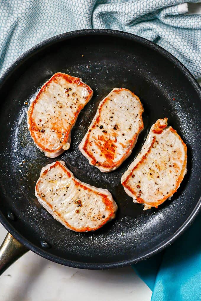 Seared pork chops in a dark skillet.