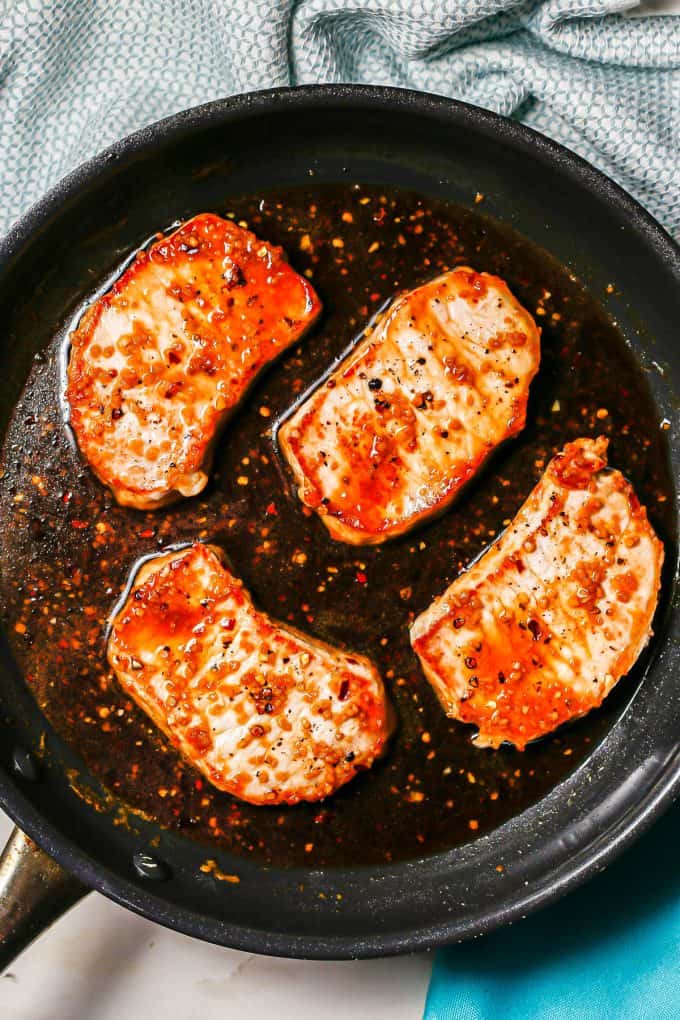 Seared pork chops in a dark skillet with a honey garlic sauce.