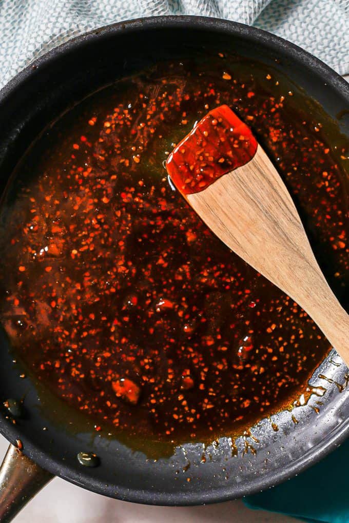 A wooden spoon resting in a soy sauce mixture in a large dark skillet being cooked and thickened.