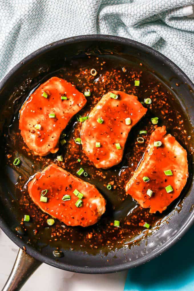 Pork chops being finished in a honey garlic sauce and topped with sliced green onions in a large dark skillet.