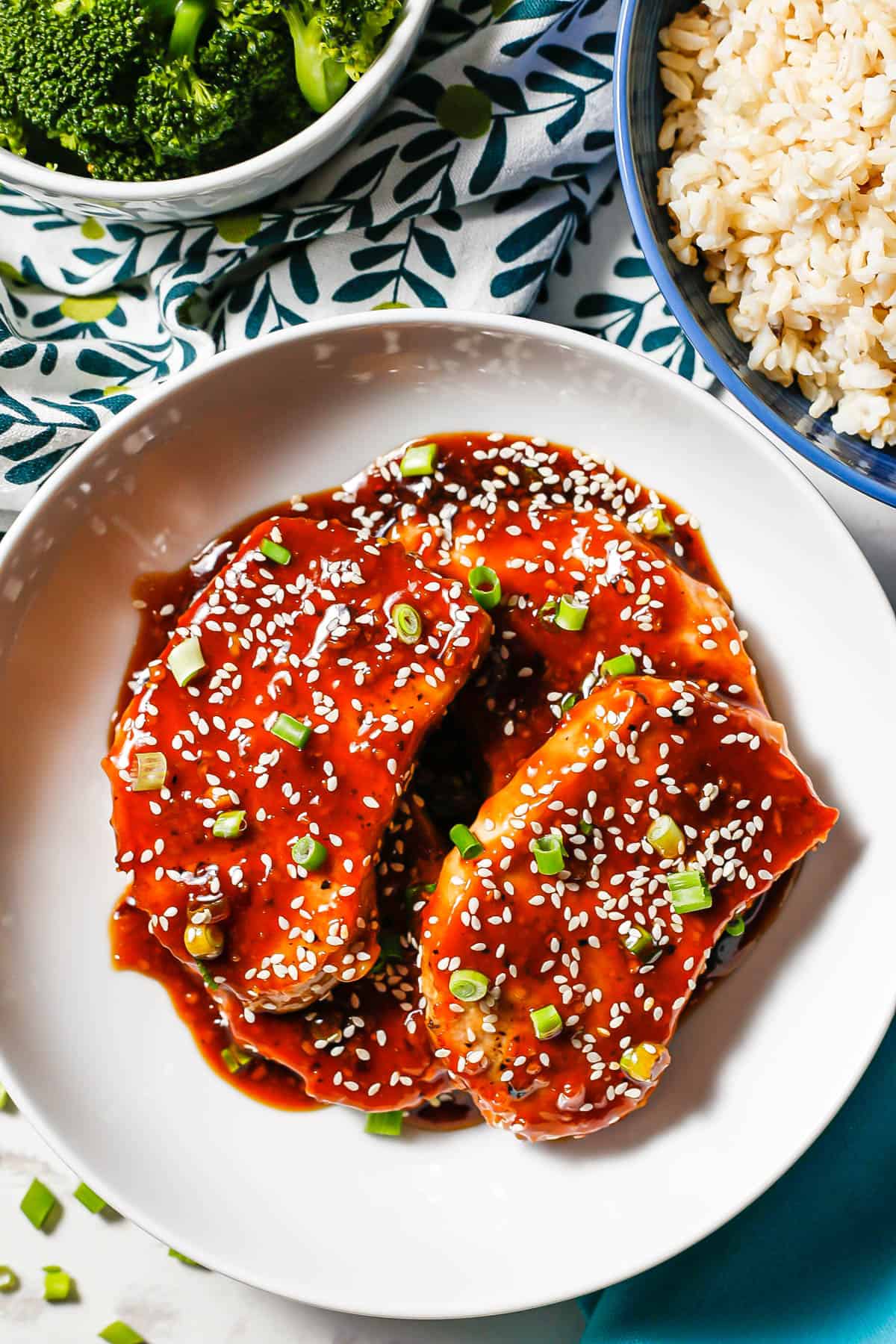 Pork chops in a low white bowl with honey garlic sauce, sesame seeds and sliced green onions.