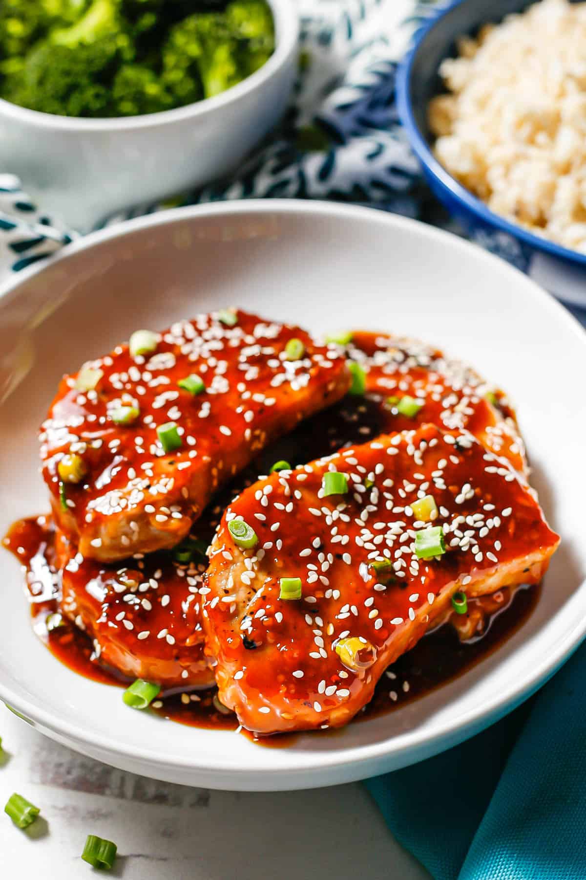 Honey garlic pork chops served in a white bowl with extra sauce and sesame seeds and sliced green onions sprinkled on top.