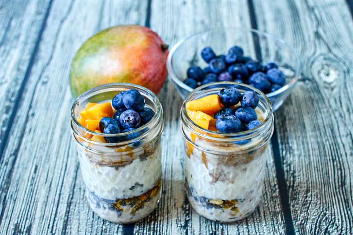 Two glass jars with overnight oats layered in and fresh fruit on top and in the background.