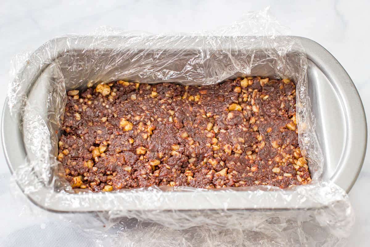 A raw date and walnut brownie mixture pressed into a small bread pan to set up before slicing.