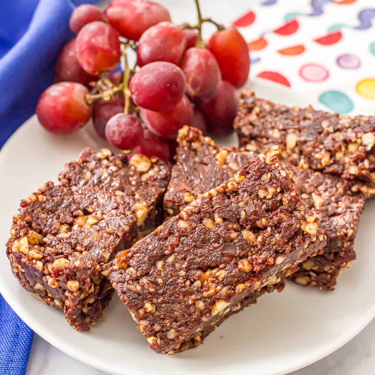 Close up of no bake brownies with walnuts on a white plate with a bunch of red grapes on the side.