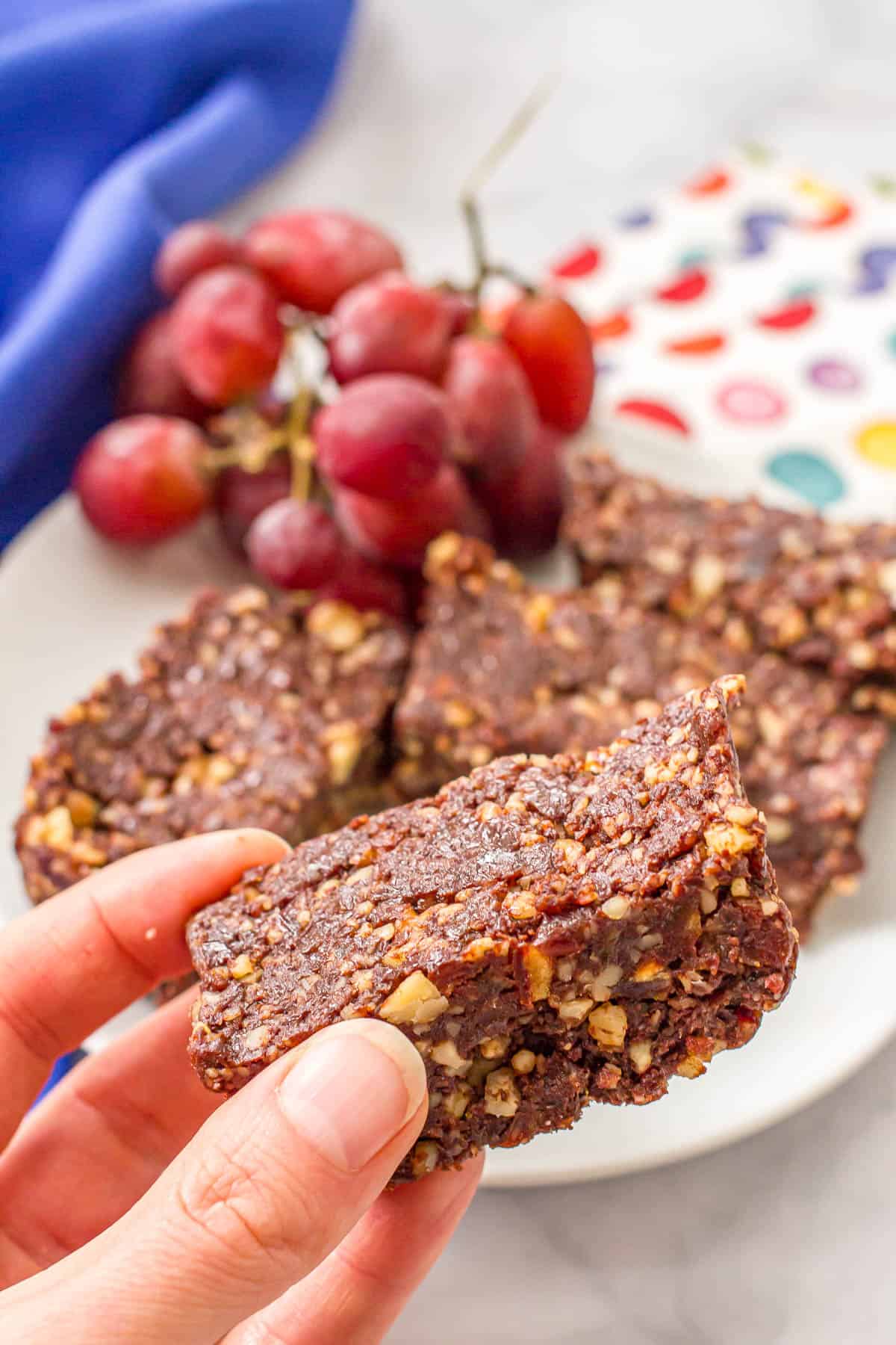 A hand holding up a thick and chewy healthy date brownie from a plate.
