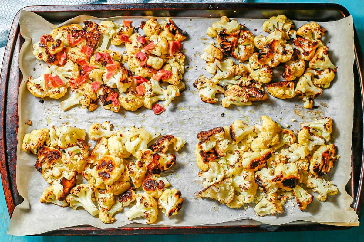A parchment paper lined baking sheet with four separate quadrants of roasted cauliflower with different seasonings and toppings.