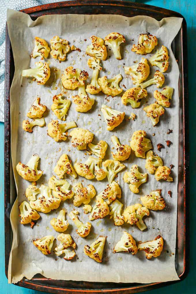 Roasted cauliflower on a parchment paper lined baking sheet.