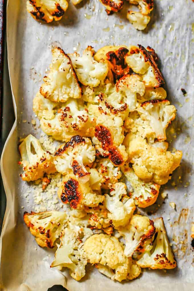 Roasted cauliflower on a baking sheet topped with grated Parmesan cheese.