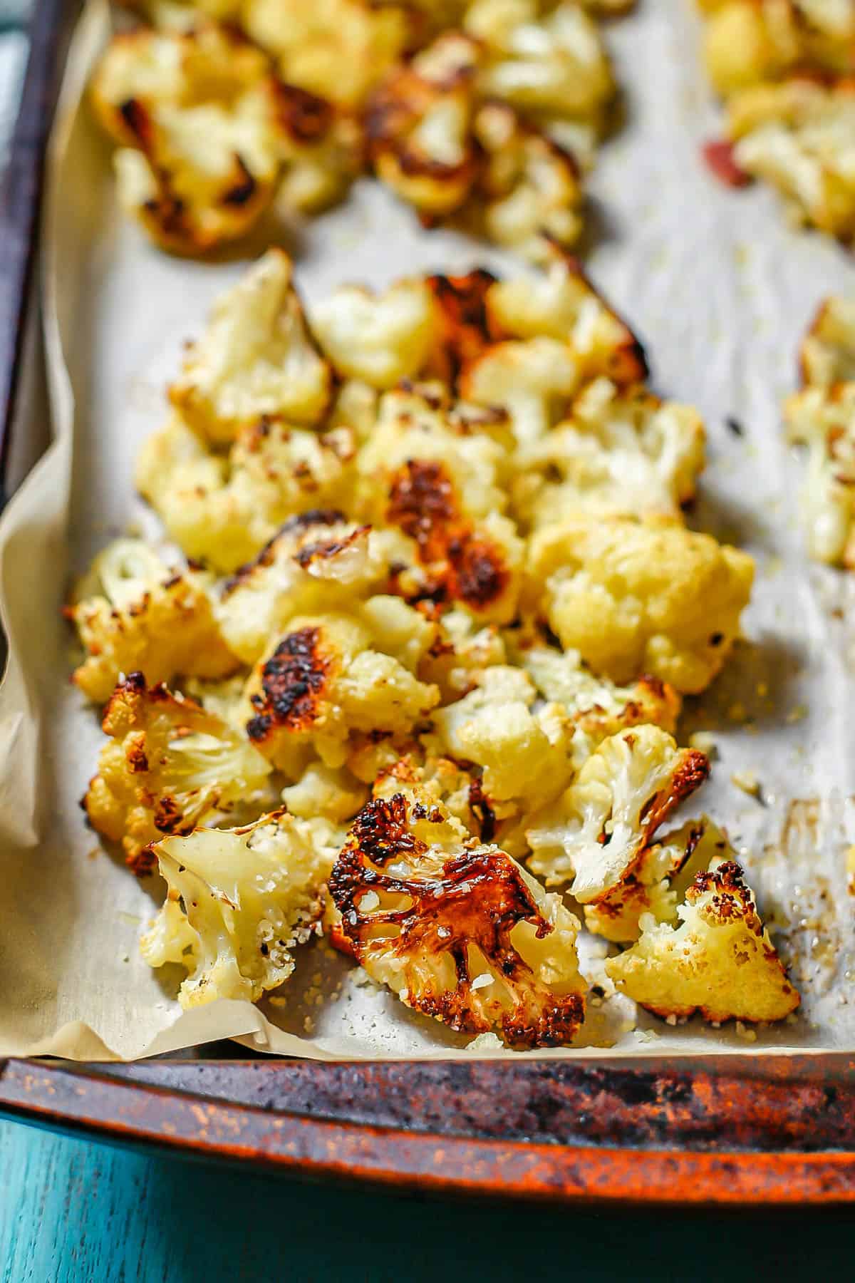 Close up of roast cauliflower with Parmesan cheese on a parchment paper lined baking sheet.