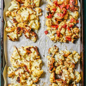 Close up of a parchment paper lined baking sheet with four quadrants of roasted cauliflower with different seasonings and toppings.