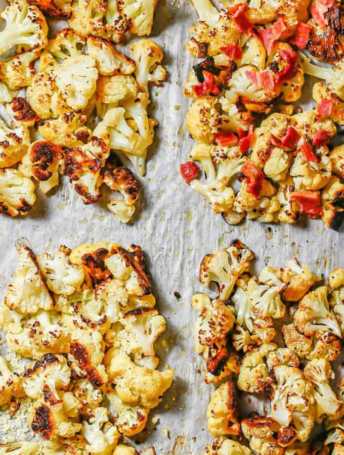 Close up of a parchment paper lined baking sheet with four quadrants of roasted cauliflower with different seasonings and toppings.