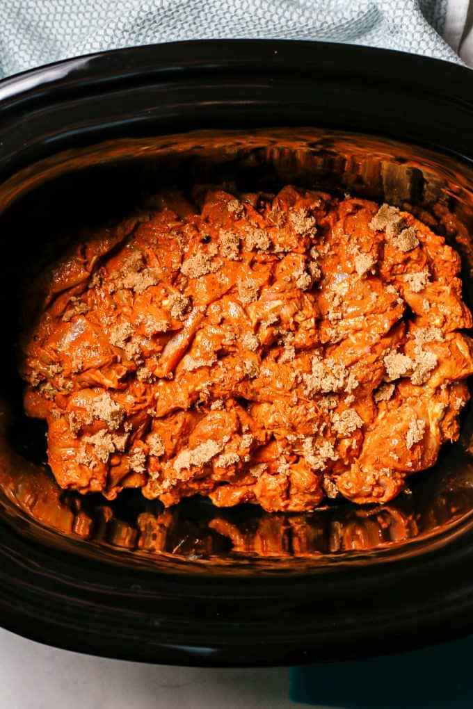 Marinated pieces of chicken thighs sprinkled with brown sugar in a slow cooker insert.